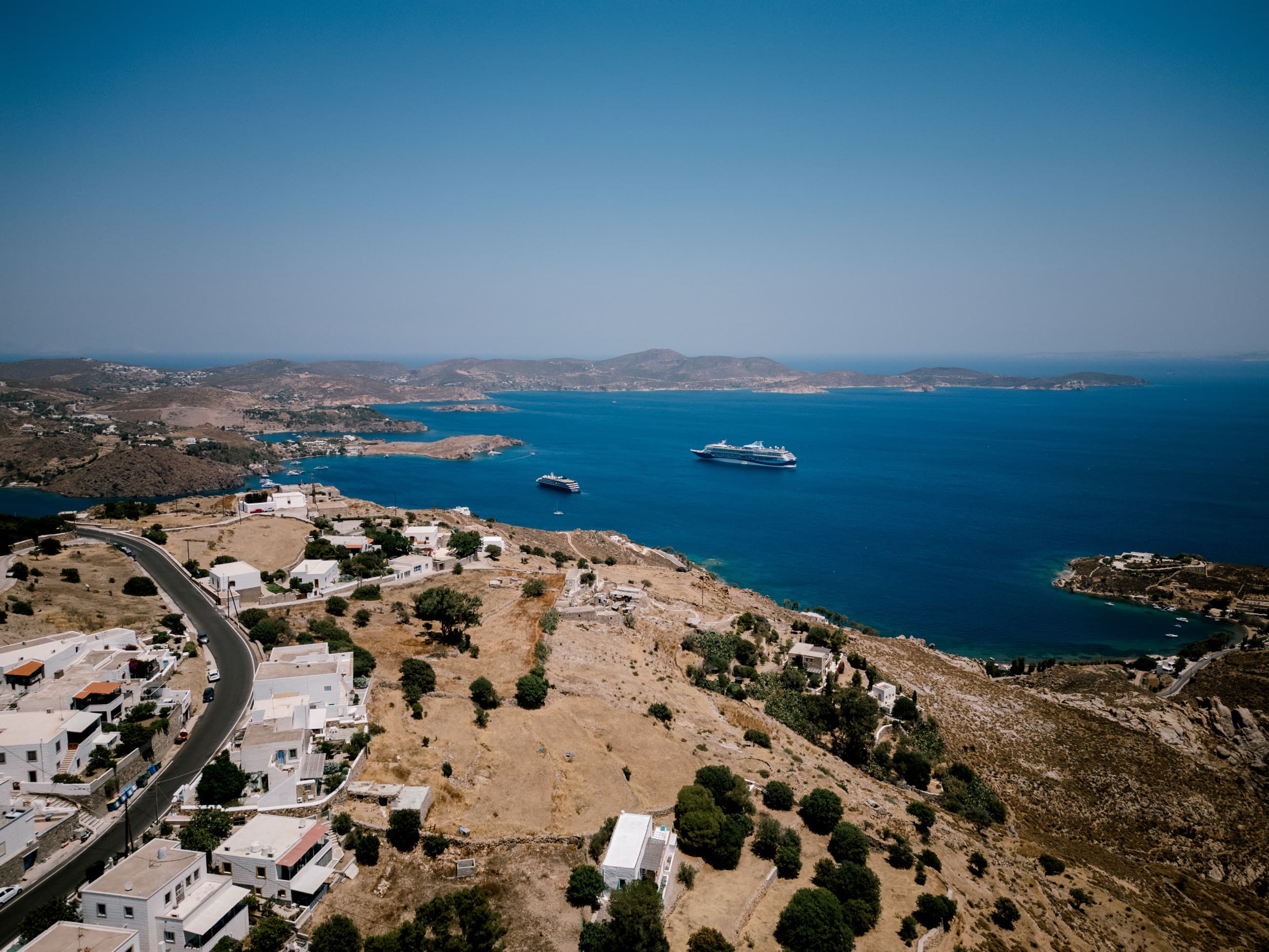 Aerial view of a bright Aegean bay, with yachts anchored off a whitewashed Greek island town